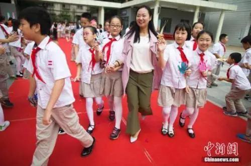 資料圖:教師節(jié),老師們牽著學(xué)生的手走過紅地毯步入校園。張?jiān)?攝